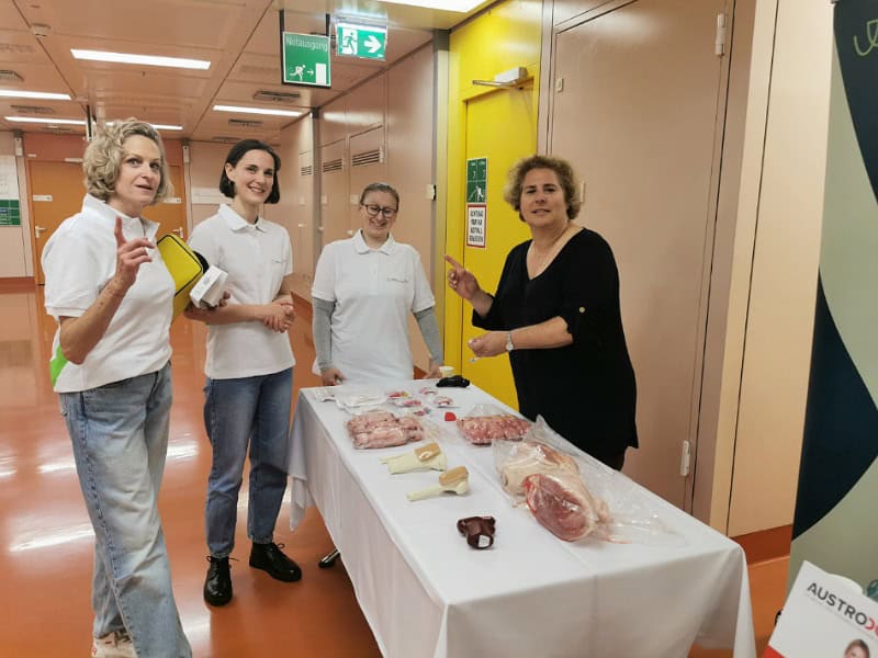 4 Ärzt:innen stehen um einen Tisch auf dem Schweinehaxen und Fleischstücke liegen, sowie Medizinprodukte mit denen man die Knochenbiopsie üben kann.